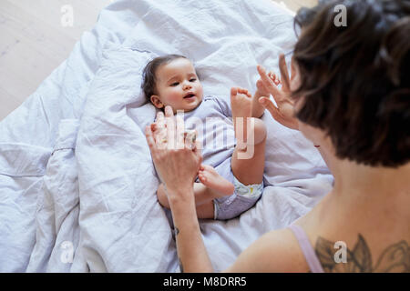Baby girl lying on bed, mother looking over her, playing Stock Photo