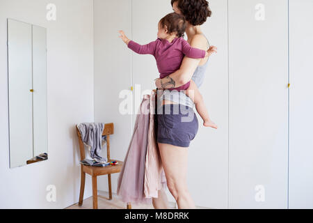 Mother holding baby girl, whilst looking in mirror, deciding what to wear Stock Photo