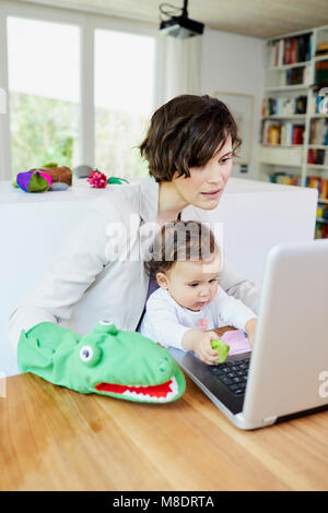 Mother using laptop with baby girl sitting on her lap Stock Photo