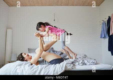 Mother and daughter playing in bedroom, mother balancing daughter on feet Stock Photo