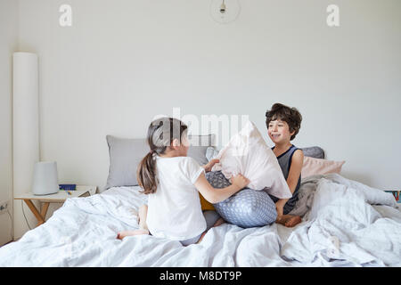 Brother and sister having pillow fight on bed Stock Photo