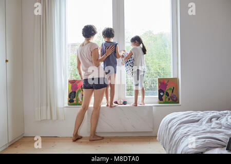 Mother, son and daughter looking out of bedroom window, rear view Stock Photo