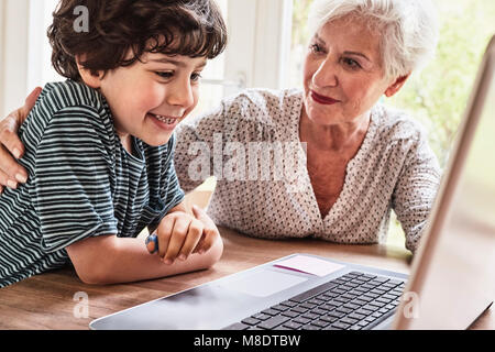 Grandmother and grandson sitting at table, using laptop Stock Photo