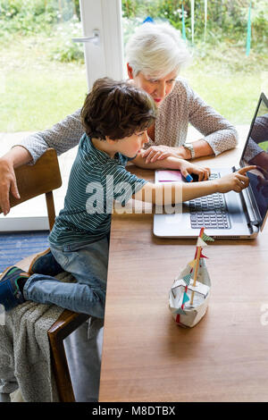 Grandmother and grandson sitting at table, using laptop Stock Photo