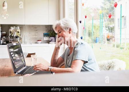 Senior woman sitting at table, using laptop Stock Photo