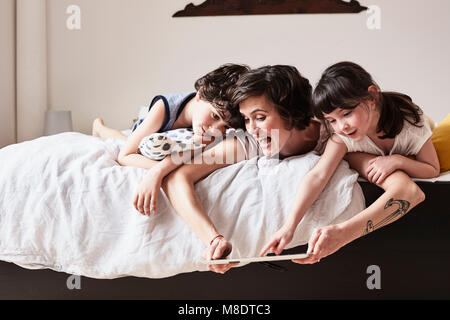 Mother, son and daughter lying on bed, using digital tablet Stock Photo