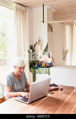 Senior woman sitting at table, using laptop Stock Photo