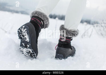 Detail on sole of black winter shoes with purple details, worn by girl walking in snowy country in winter. Stock Photo
