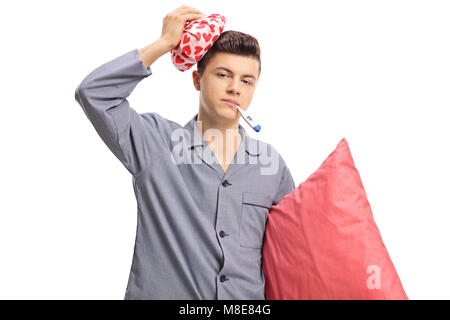 Sick teenage boy in pajamas holding an icepack on his head and a thermometer in his mouth isolated on white background Stock Photo