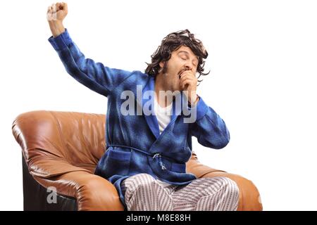 Sleepy man sitting in an armchair and yawning isolated on white background Stock Photo