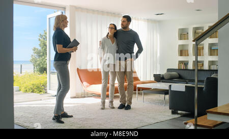 Professional Real Estate Agent Shows Stylish Modern House to a Beautiful Young Couple Who are in the Market for Purchasing/ Renting New Home. Stock Photo