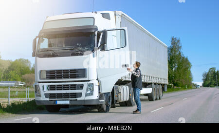 Truck Driver Gets out of His Parked White Cab-Over Truck. Day is Sunny, Driver is Professional. Stock Photo