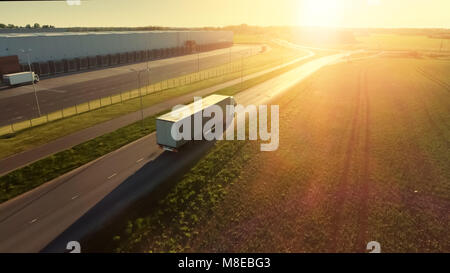 Aerial Shot of White Semi Truck with Cargo Trailer Attached Moving Through Industrial Warehouse, Rural Area. Sun Shines and the Sky Are Blue. Stock Photo