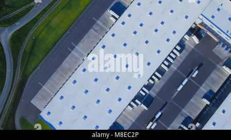 Aerial Top View of Industrial Warehouse/ Storage Building/ Loading Area with Solar Panels on the Roof and Many Trucks Loading/ Unloading Merchandise. Stock Photo