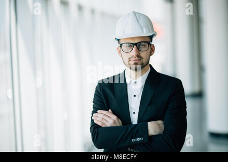 Successful engineer or architect, Joyous businessman with crossed arms wearing helmet on office background Stock Photo
