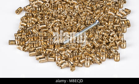 Bronze threaded inserts on white background. Close-up of pile of golden metal parts with a long silvery bolt. Construction, build, store, engineering. Stock Photo
