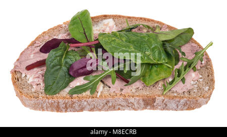 Slice of bread with pate and fresh herbs. Homemade snack decorated with leaves of spinach, chard, arugula and red beet. Isolated on white background. Stock Photo
