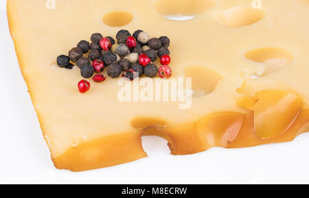 Piece of smoked hard cheese with colorful pepper corns. Beautiful close-up of edam with holes and heap of peppercorn mixture on a white background. Stock Photo