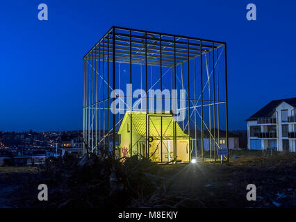 14 March 2018, Germany, Pforzheim: The art project 'The threatened house' (German: 'Das bedrohte Haus') pictured painted in yellow, lit and amidst high cage bars. The small, empty one-room house was turned into an art installation by artist and engineer Andreas Sarow. According to Sarow himself, his aim with this project is to call attention on 'the new things that are coming and what we must give up in exchange'. He also criticizes bourgeois construction design. Photo: Uli Deck/dpa Stock Photo