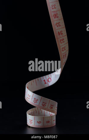 Coiled Tailors tape measure showing centimetres and Inches close up black background Stock Photo