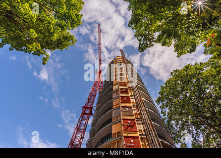 view from below upwards on the construction of a tower crane, a multi-storey building on a summer day against a blue sky and white clouds Stock Photo