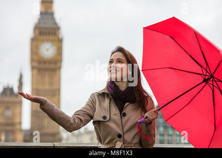 Girl or young woman with a red umbrella, hand out, checking for rain by Big Ben, London, England, Great Britain Stock Photo