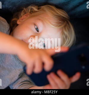 Little boy (2-3) lying down and playing game on smart phone Stock Photo