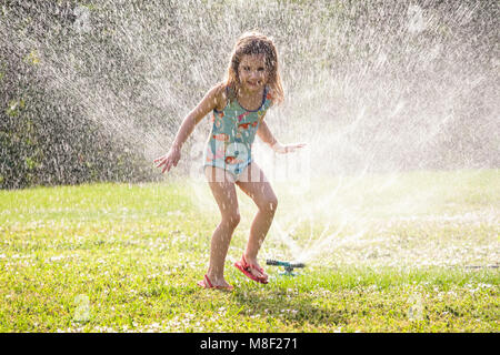 Girl (4-5) splashing in sprinkler water on lawn Stock Photo