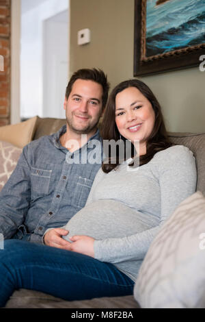 Mid adult couple sitting on sofa and smiling to camera Stock Photo