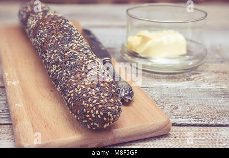 Rye bread with seeds of hemp and a kino. Healthy bread. Baguette and table knife and butter. Wooden background Clouse-up Stock Photo