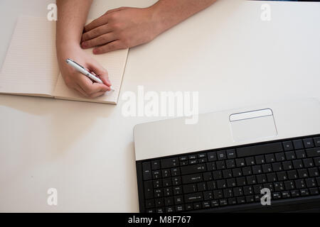 Right hand writing on notebook next to the laptop on desk