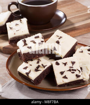 Pile of chocolate fudge brownies on a plate with a cup of coffee in background Stock Photo
