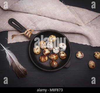 raw quail eggs in a round black cast-iron frying pan on a black table, top view, vintage toning Stock Photo
