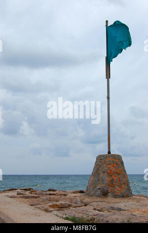 Green beach flag in good weather with sea background in the coast of Sitges, province of Barcelona. Spain. Stock Photo