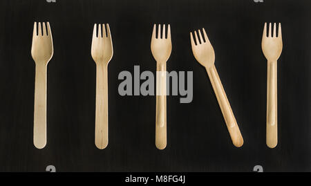 Disposable wooden ecologically designed forks and spoons for takeout meal, food to-go on the black background. Conceptual. Stock Photo