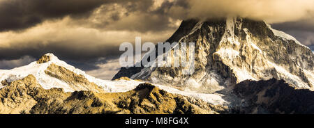 bad weather and storm clouds over high snow-capped mountain landscape in golden evening light Stock Photo