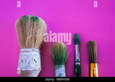 Brushes of different sizes, used and dirty isolated on pink background with vibrant colors. Stock Photo