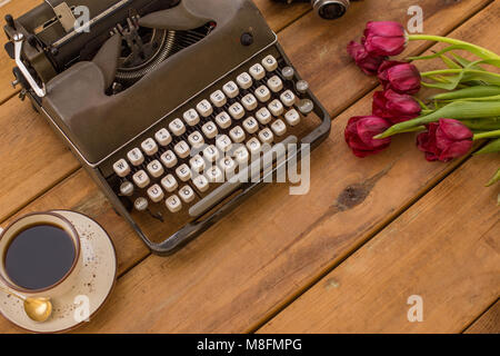 Writing in spring. Flatlay with retro typewriter, wine-red tulips and a cup of coffee on wooden background with negative space. Stock Photo
