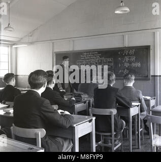 1950, historical, male A-level students in a classroom sitting an individual wooden being taught statistical measurement - the correlation coefficient - by a male teacher at a blackboard wearing a formal gown over his jacket England, UK. Stock Photo