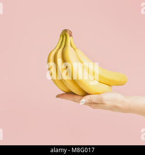 Female hand holding bunch of bananas at pastel pink background, front view Stock Photo