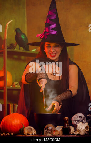 Portrait of witch in black hat with magic wand and cauldron Stock Photo