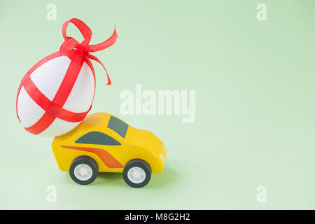 Yellow toy car carrying a decorated easter egg. Stock Photo