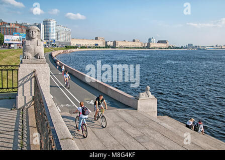 People ride bicycles next to the sculptures of sphinxes on Sverdlovskaya Embankment near The Neva River Stock Photo