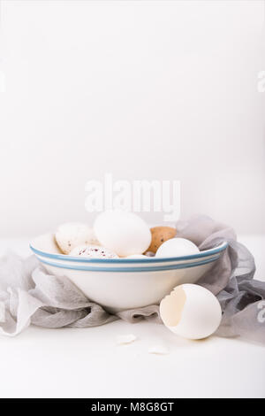 White eggs in bowl, broken egg shell and silk fabric on a white table and white background. Easter concept. Stock Photo