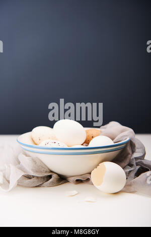 White eggs in bowl, broken egg shell and silk fabric on a white table and dark background. Easter concept. Stock Photo
