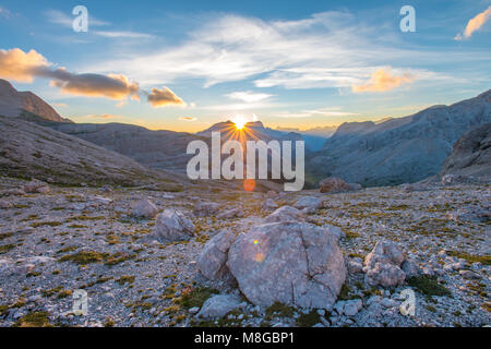 Beautiful painted sky, clouds as the sun comes out from behind the mountains at the horizon. Sunrise in the Dolomites, Alps in Northern Italy. Stock Photo