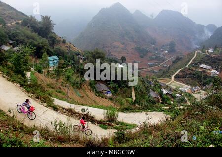 Ha Giang, Vietnam - March 18, 2018: Children driving bicycles in a village surrounded by mountains and fog in the northernmost province of Vietnam Stock Photo