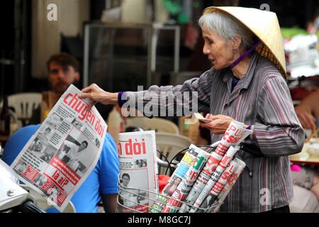 Hanoi, Vietnam - March 15, 2018: Senior lady selling local newspapers with a bicycle Stock Photo