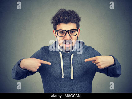 Young angry man in eyeglasses overreacting while pointing at himself looking offended. Stock Photo