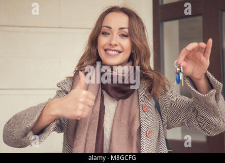 Young smiling girl holding keys from new real estate showing thumb up outdoors. Stock Photo